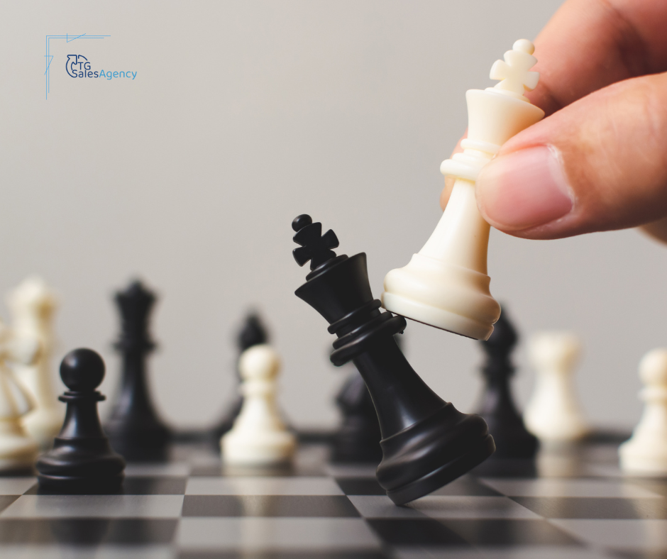 Hand moving a white king chess piece to knock over a black king, symbolizing how to evaluate your sales strategy in B2B sales.